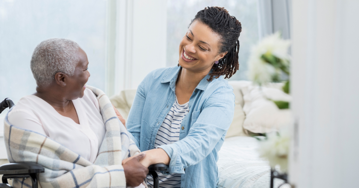 Adult daughter smiling and holding the hand of her aging mother as they discuss home care assistance options.