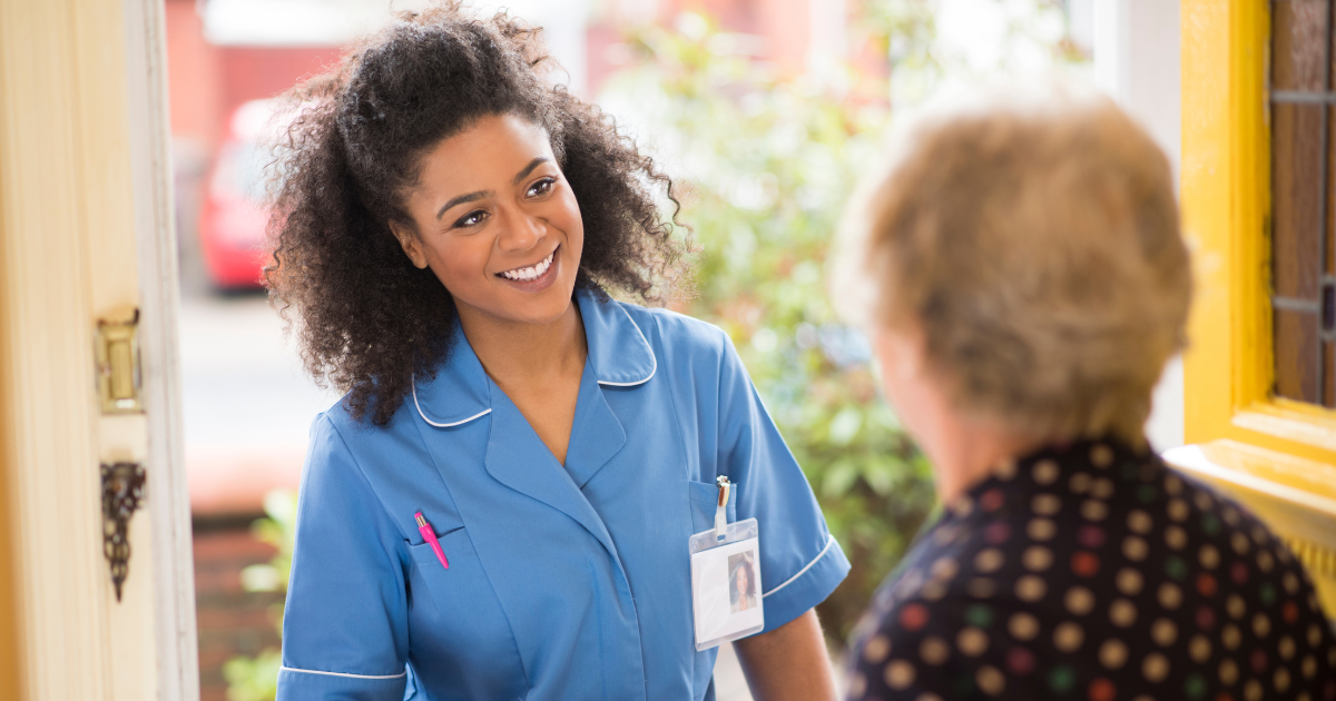 Elderly woman opens the door to her smiling professional caregiver