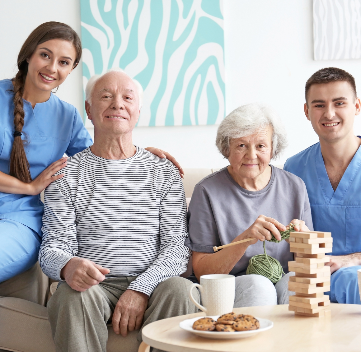 2 professional caregivers embrace an elderly couple, representing the positive effect that personal care in Lexington, VA can have.