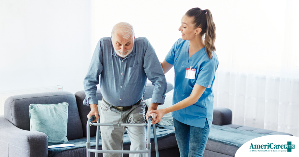 A professional caregiver helps an older man walk with a walker, showing how having a caregiver help a loved one stay mobile safely can help avoid hospital readmissions.