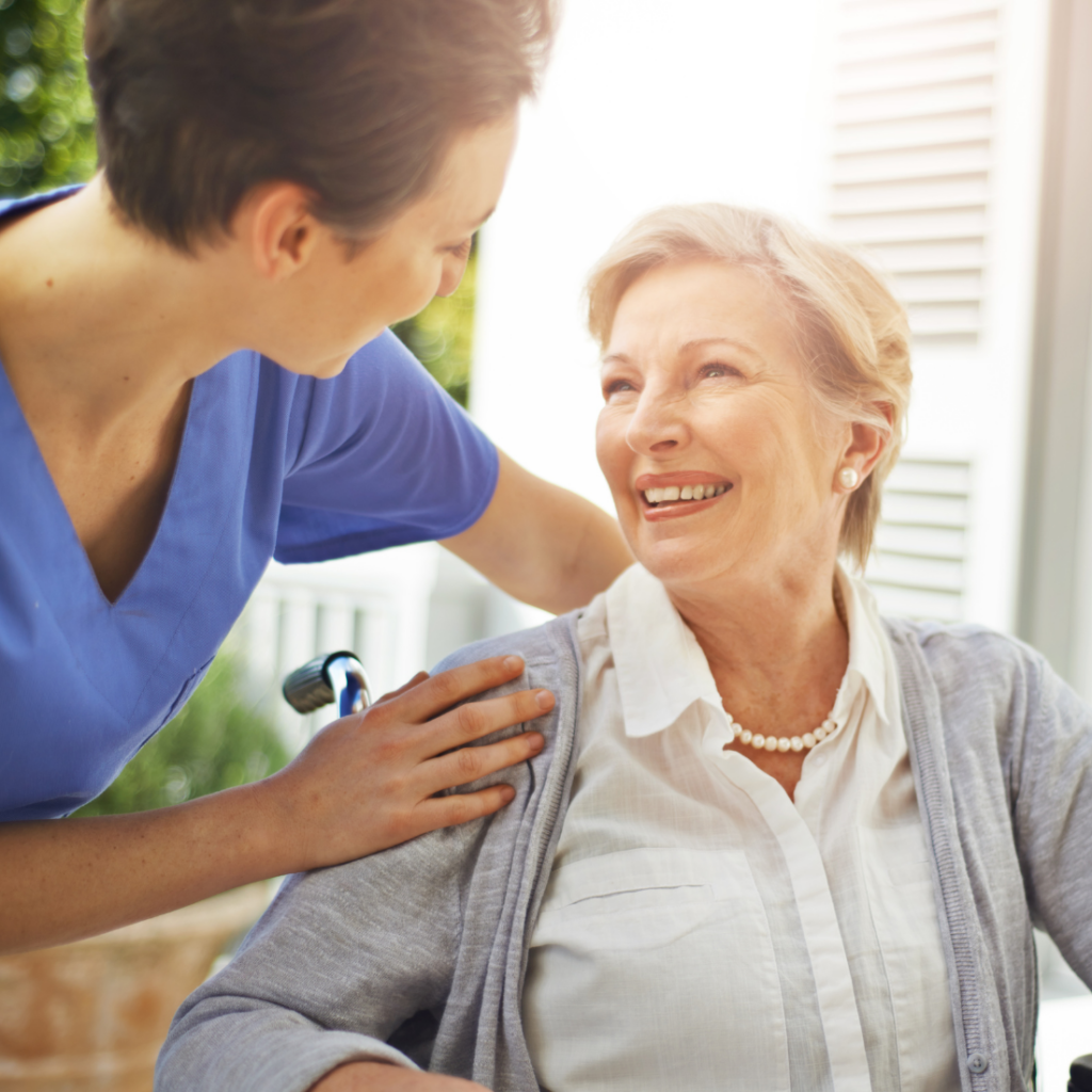 A professional caregiver helps a senior client as they both smile, representing how companion care in Mecklenburg County can help.