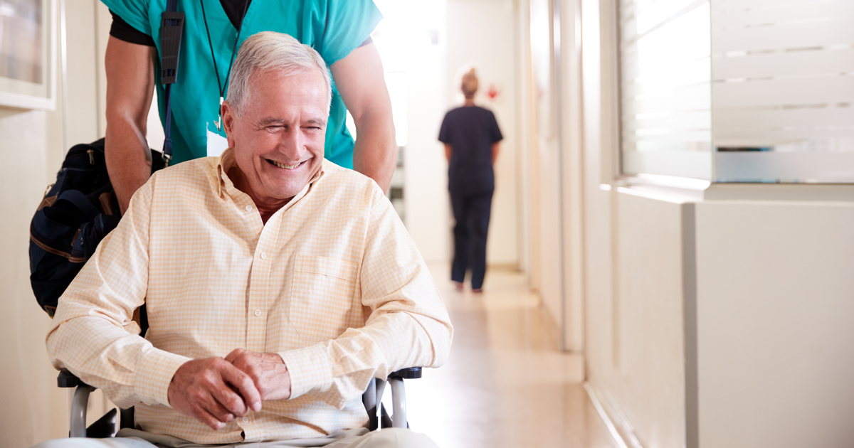 A caregiver wheeling an older adult out of a facility represents Post Operative Care in Mecklenburg