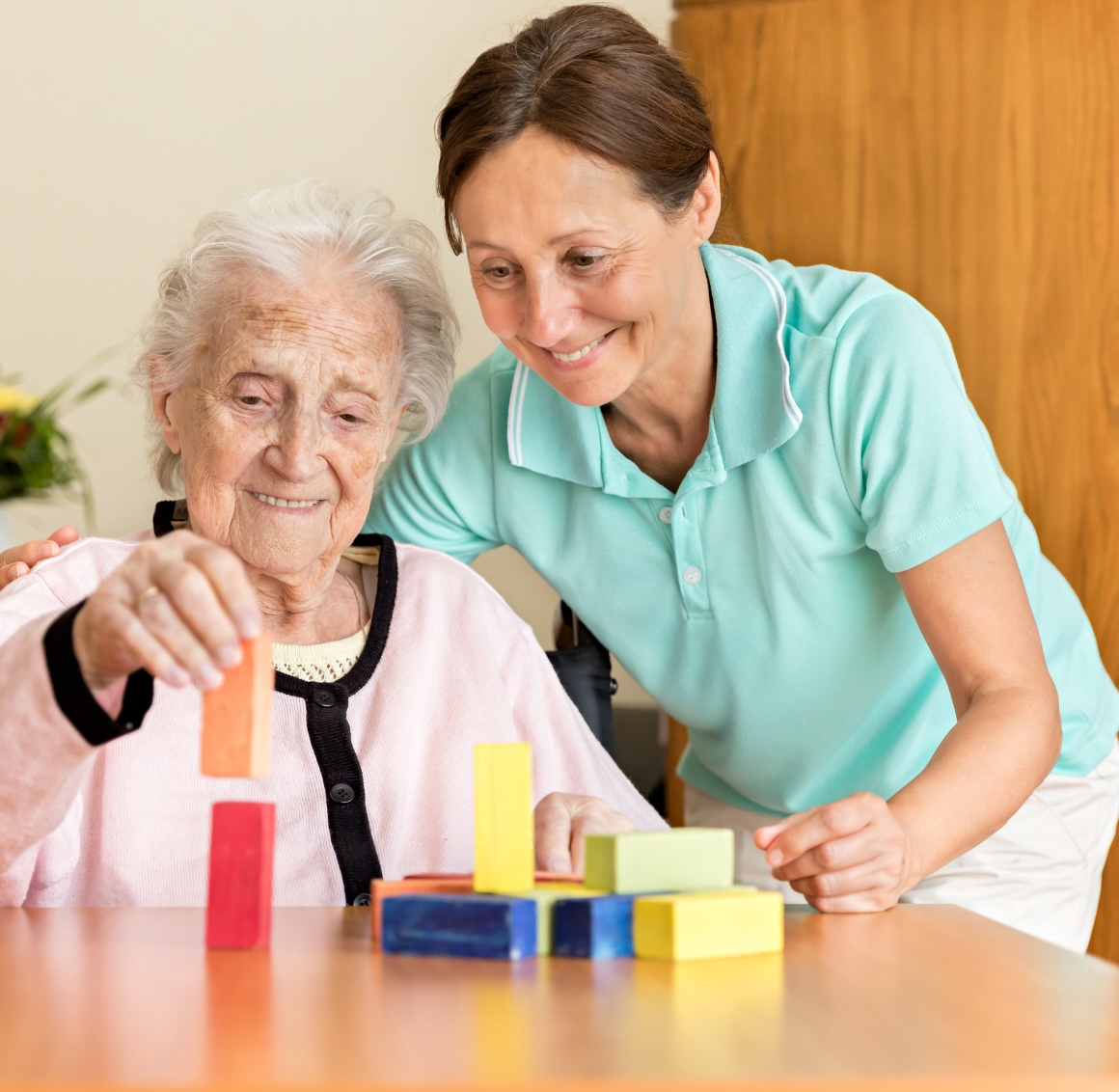 A caregiver helps a older client with a block activity to help keep her sharp, representing how dementia care in Orange can help.