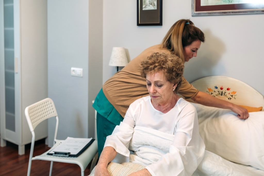 Personal Care Orange A caregiver helps an older client get comfortable in bed, representing how personal care in Orange can help!