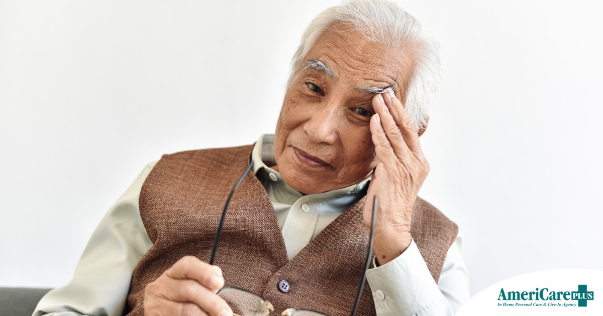 An older adult holds his head and his glasses representing vision problems like macular degeneration.