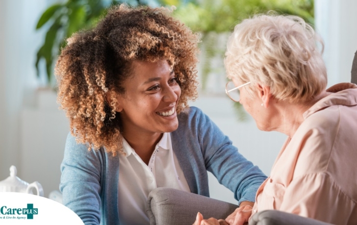 A caregiver smiles at an older client in a chair, representing the joy that can come from a healthy work-life balance.
