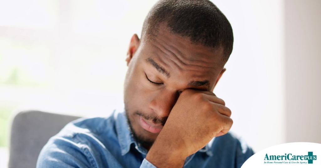 A man tiredly rubs his eyes, representing the exhaustion that can come with family caregiving.