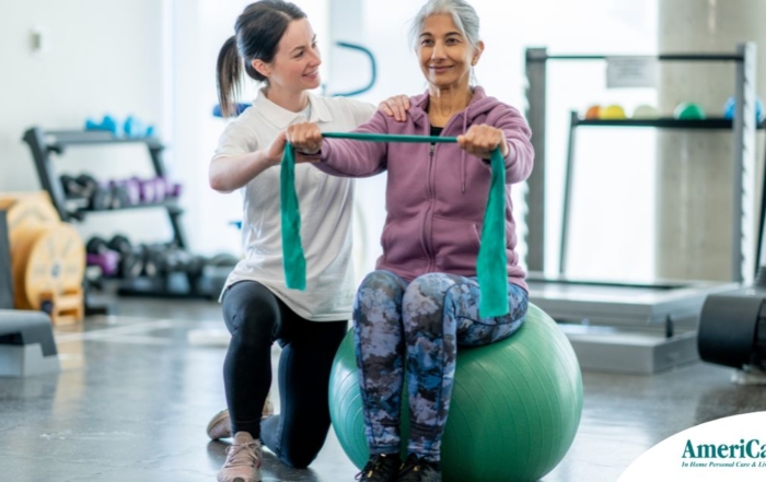 A care provider helps an older woman exercise with a resistance band and an exercise ball, representing how exercise can help with senior fall prevention.